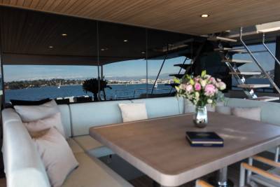 A vase of flowers sits on a table in the foreground, with a scenic view of a bay and distant hills visible through large windows in the background.