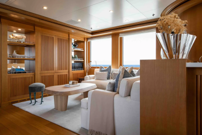 A plush white sofa with blue and white pillows sits in the foreground of a wood-paneled living area with large windows overlooking the ocean in the background.