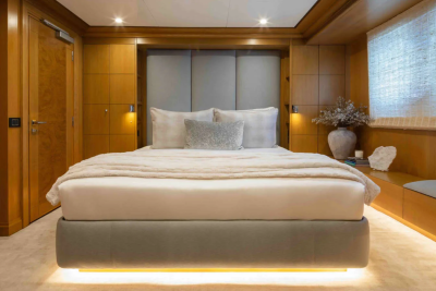 A luxurious bedroom with a plush bed in the foreground and warm wood paneling and a window with blinds in the background.