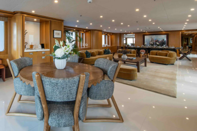 A round dining table with upholstered chairs sits in the foreground, while a spacious lounge area with sofas and artwork is visible in the background.