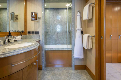 A luxurious bathroom features a granite countertop with a sink in the foreground, and a glass-enclosed shower and wooden cabinets in the background.