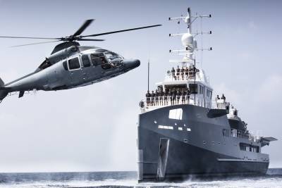 A helicopter flies over a large yacht sailing on the ocean.