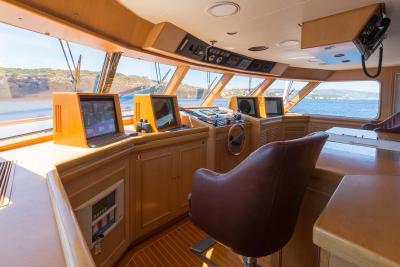 A luxurious yacht's bridge, with a captain's chair in the foreground and a scenic ocean view through the windows in the background.