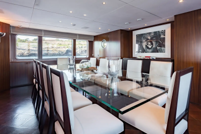 A long, polished dining table with white chairs fills the foreground, while a large framed photograph hangs on the wood-paneled wall in the background.