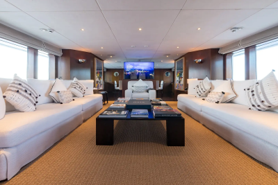 Two plush white sofas with decorative pillows flank a dark coffee table filled with books, while a large screen displays a city skyline in the background.
