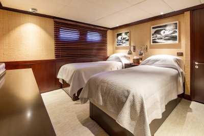 Two neatly made twin beds with white linens fill the room, while a dark wood dresser and door frame the space in the foreground and background.