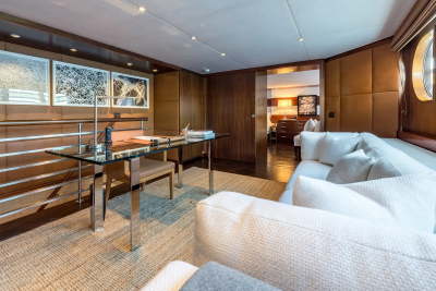 A modern office space with a glass desk and chair in the foreground, and a plush sofa and a glimpse into a bedroom in the background.
