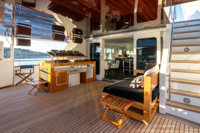 A DJ setup and lounge area with a reflective ceiling are on the deck of a yacht, with a glimpse of an interior dining area and the sea in the background.