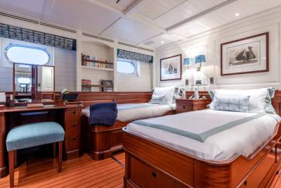 Two neatly made beds with blue accents are in the foreground, while a wooden desk with a blue stool and framed nautical art adorn the background of this luxurious cabin.