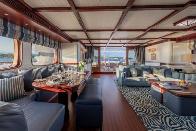 A luxurious yacht interior features a formal dining table in the foreground and a spacious lounge area with a view of the ocean in the background.