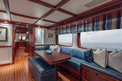 A luxurious yacht interior features a U-shaped blue leather banquette with a wooden table in the foreground, while the background reveals a large window overlooking the calm ocean.