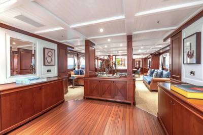A luxurious yacht interior features polished wooden floors and cabinetry in the foreground, with plush seating areas and large windows visible in the background.