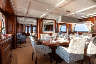 A formal dining table set for a meal is in the foreground, with a lounge area visible in the background through an open doorway.