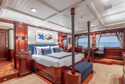 A luxurious yacht bedroom with a large bed in the foreground and a view of the ocean through the windows in the background.