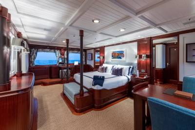 A luxurious bedroom with a large bed and seating area in the foreground, and windows overlooking the ocean in the background.