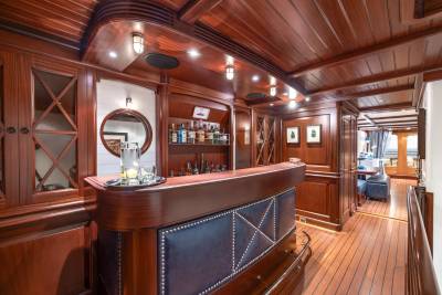 A polished wooden bar with a leather front is in the foreground, while a hallway with more wood paneling and a glimpse of a dining area is in the background.