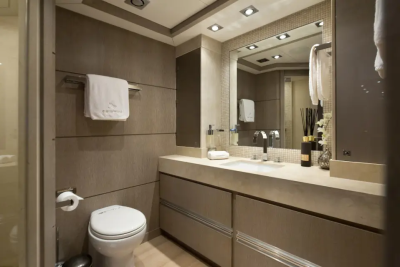 A modern bathroom features a toilet and towel rack in the foreground, with a vanity, sink, and mirror in the background.