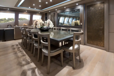 A long, polished dining table with chairs is set in a luxurious room with large windows overlooking a green landscape in the background.