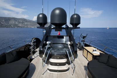 A luxurious yacht with a hot tub and lounge chairs in the foreground is at sea with a mountainous coastline in the background.