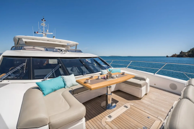 A luxurious yacht's deck, furnished with plush seating and a dining table, overlooks a tranquil blue ocean with a distant, rocky island under a clear sky.