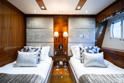 Two neatly made beds with patterned pillows fill the foreground, while the background features wood-paneled walls and a window with a view of the sky.