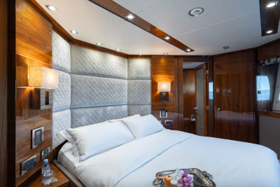 A luxurious bedroom with a plush white bed in the foreground and warm wood paneling and a doorway in the background.