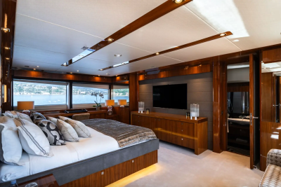 A luxurious bedroom with a large bed in the foreground and a large television and windows overlooking a body of water in the background.