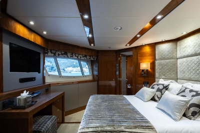 A luxurious yacht bedroom features a plush bed in the foreground and a large window with a view of a coastal town in the background.