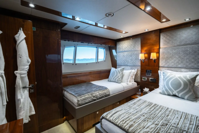Two beds with patterned bedding are in the foreground, while a window with a view of the sea and sky is in the background.