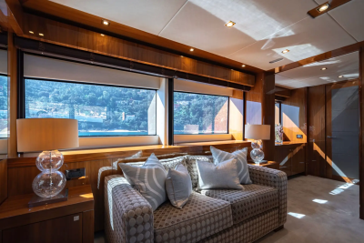 A plush sofa with decorative pillows sits in the foreground, while large windows in the background reveal a scenic view of a coastline.