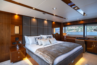 A luxurious yacht bedroom with a large bed in the foreground and a scenic view of a coastal town through the window in the background.