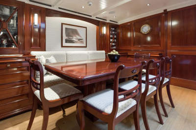 A polished wooden dining table with chairs is set in a richly paneled room with a built-in banquette and artwork on the wall.