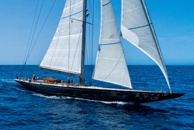 A majestic dark sailboat with full sails glides across the deep blue ocean under a clear sky.