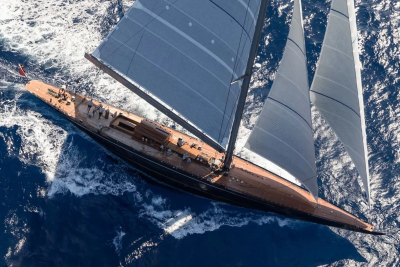 A sleek wooden sailboat with dark sails glides through choppy blue water.