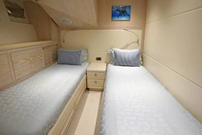 Two neatly made twin beds with blue pillows sit in a well-lit cabin, with a small framed picture of an elephant above the headboard.