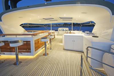 A well-lit bar area with stools on a yacht's deck overlooks a calm body of water with distant buildings.