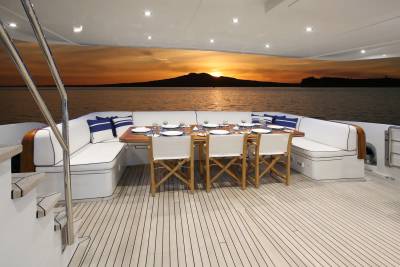 A set dining table on a yacht's deck faces a vibrant sunset over the ocean.
