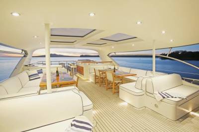 Luxurious white seating and dining areas on a yacht's deck overlook a calm, blue ocean at dusk.