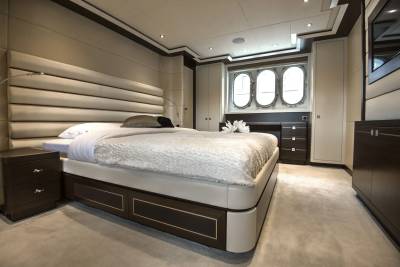 A luxurious bedroom with a large bed in the foreground and oval windows in the background.