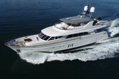 A sleek white yacht cruises through dark blue water, leaving a foamy wake behind it under a clear sky.