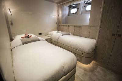 Two neatly made beds with a stuffed animal on one are in the foreground, while the background features porthole windows and wooden cabinetry.