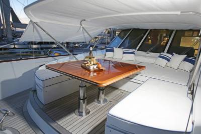 A polished wooden table with champagne bottles sits on a yacht's deck, with other boats docked in the background.