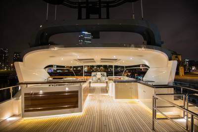 A luxurious yacht deck with illuminated wooden flooring in the foreground is set against a backdrop of a city skyline at night.