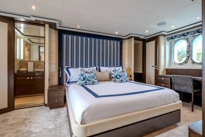 A luxurious bedroom with a large bed in the foreground and a desk with windows overlooking the sea in the background.