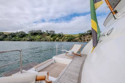 Two lounge chairs sit on the deck of a yacht with a lush, green coastline in the background.