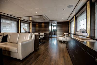 A luxurious yacht interior features a cream-colored sofa in the foreground and a model yacht on a dark cabinet in the background.
