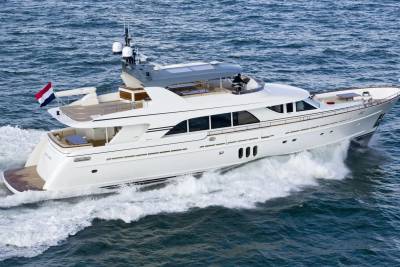 A white luxury yacht cruises through choppy blue water, leaving a foamy wake behind it, with a clear sky visible in the distance.