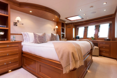 A luxurious master stateroom on a yacht features a large bed with plush pillows in the foreground and large windows offering a view of the sea in the background.