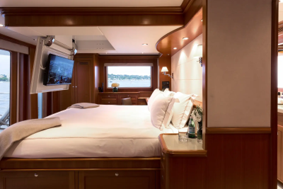 A luxurious yacht bedroom with a large bed in the foreground and a scenic view of water and trees through a window in the background.