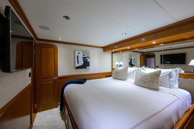 A luxurious yacht bedroom features a large, made-up bed in the foreground and a mirrored wall reflecting the room and a television in the background.